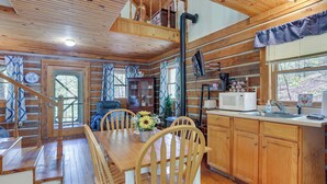 Ein Holzblockhaus-Interieur mit Essbereich, Küche und einer Treppe, die zu einem Schlafboden führt.
