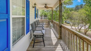 A wooden porch with blue shutters, a ceiling fan, and a view of trees and a car in the background.