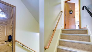 Eine Holztür mit Schlüsselloch und Griff, ein Holzterrassengeländer und eine Teppichstufen Treppe mit Holzbalkon und schwarzem Geländer.