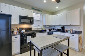 Una cucina moderna con mobili bianchi, un frigorifero in acciaio inossidabile, un forno a microonde, un piano cottura e una macchina da caffè.
