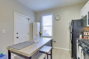 A small kitchen with a wooden table, a refrigerator, and a window with blinds.