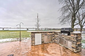 An outdoor kitchen with a grill, a refrigerator, and a stone wall.