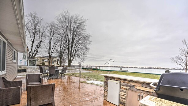 An outdoor patio with wicker furniture, a stone grill station, and a view of a body of water and a bridge. - Waterfront East China Home w/ Dock & Patio! (East China)