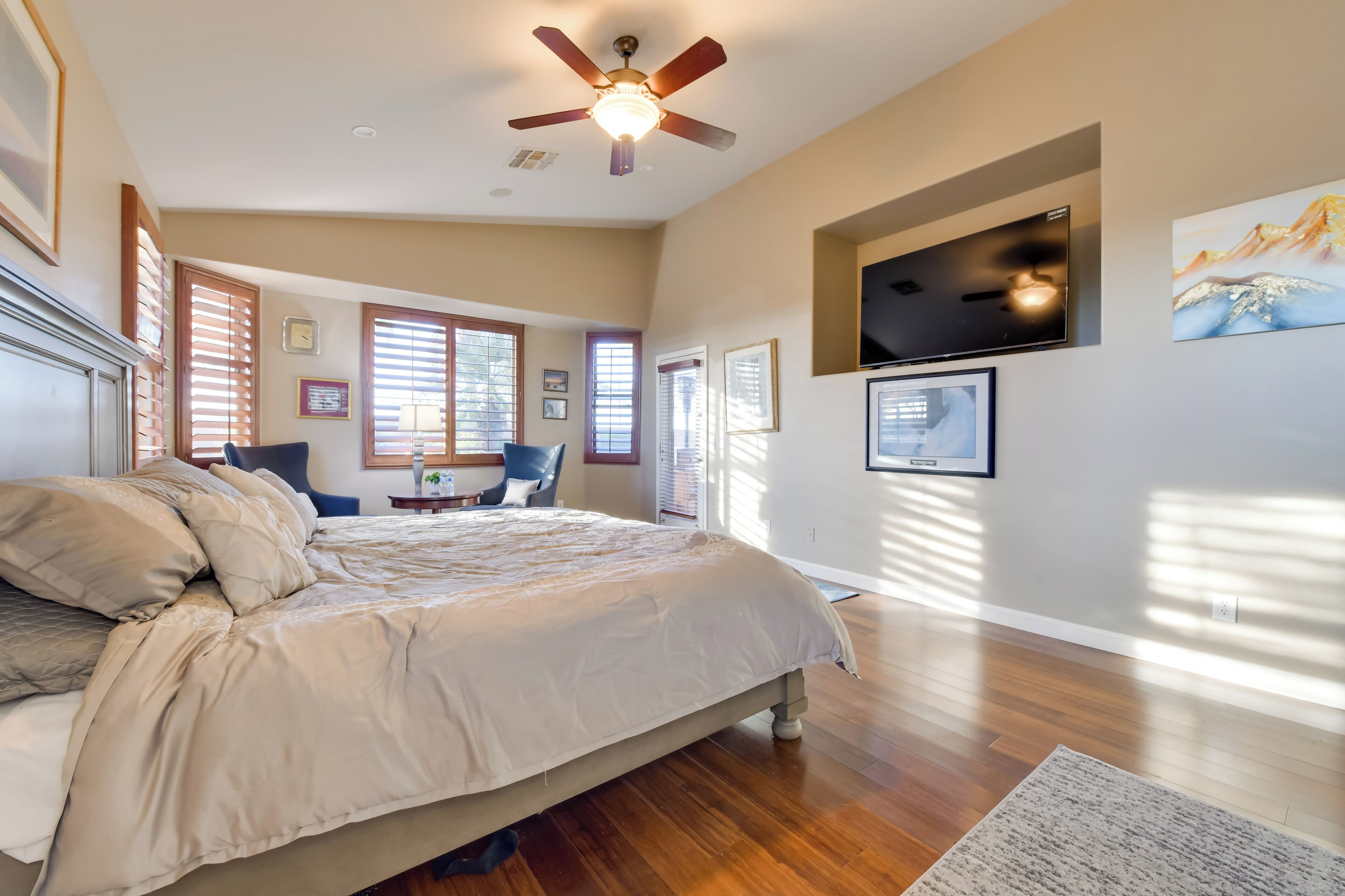 A bedroom with a large bed, a ceiling fan, a flat-screen TV, and a painting on the wall.