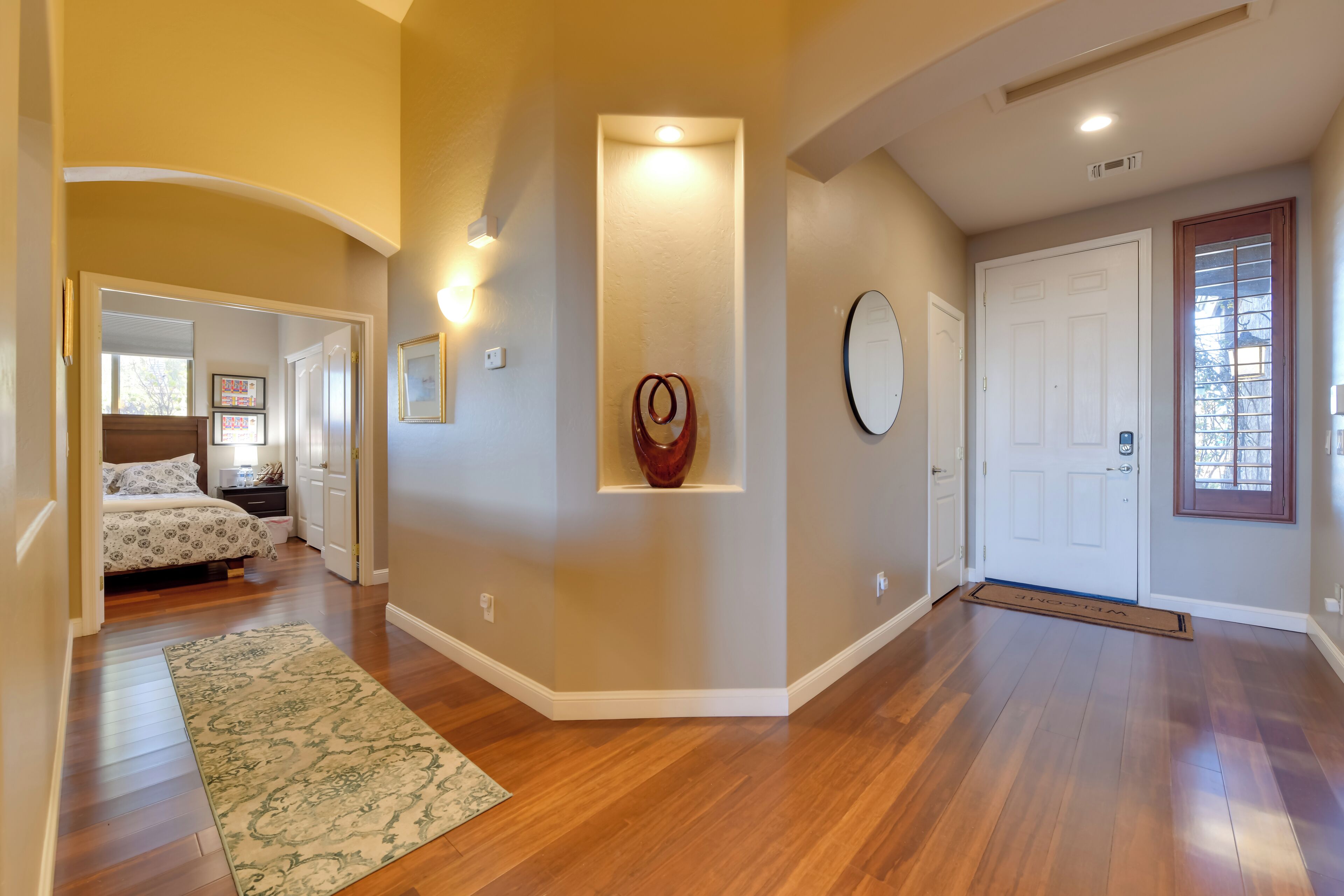 A spacious hallway with wooden flooring, a decorative rug, and a door with a doormat.