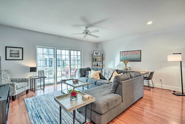 A modern living room with a grey sectional sofa, a coffee table, and a dining area with a table and chairs. - Patio & Pool Access: Rehoboth Beach Retreat (Rehoboth Beach)