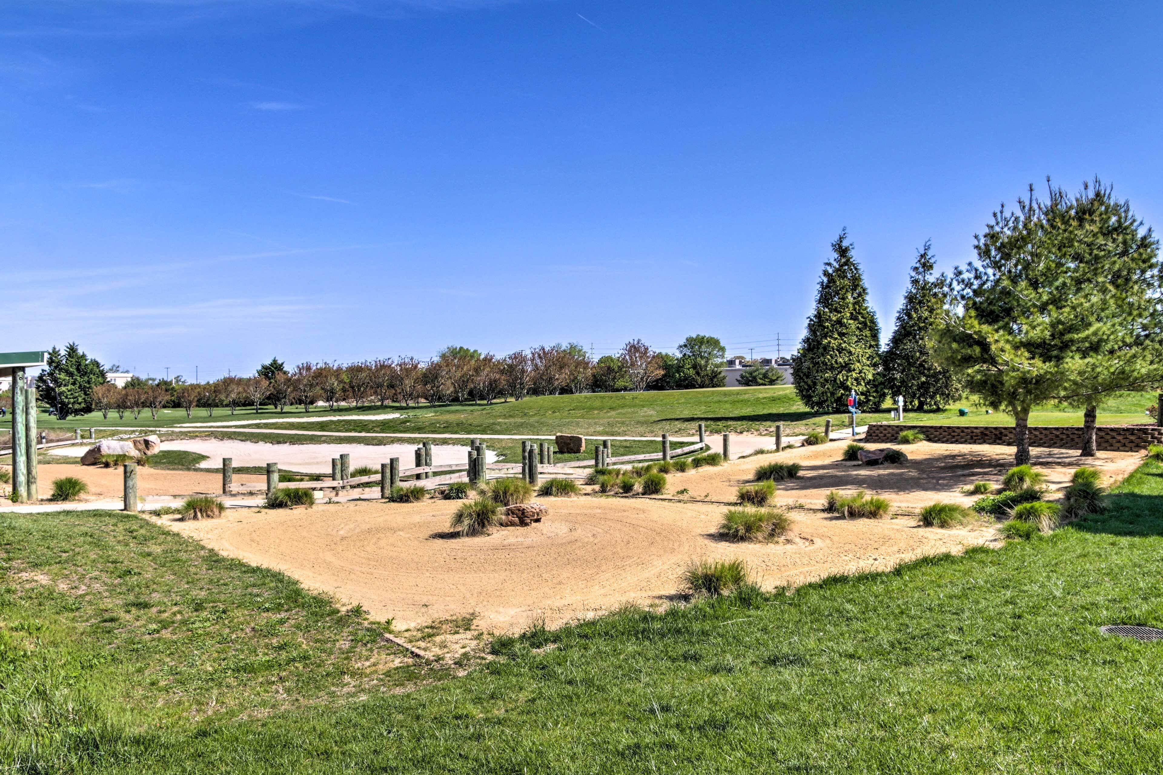 Ein Golfplatz mit Sandbunkern, einem Holzzaun und einem großen Baum.