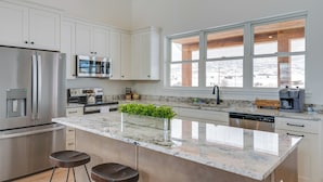 Une cuisine moderne avec des meubles blancs, des appareils en acier inoxydable, une grande fenêtre et un plan de travail en marbre.