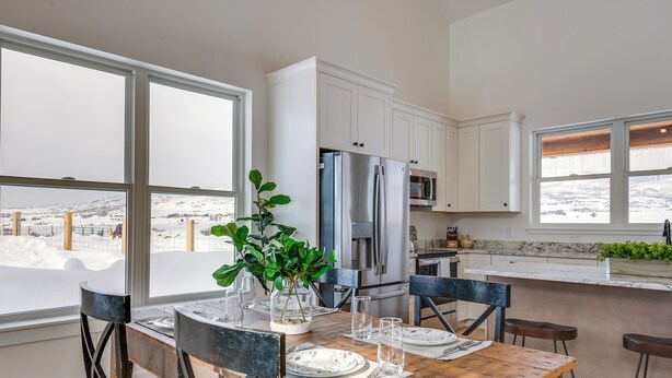 Une cuisine moderne avec des meubles blancs, des appareils en acier inoxydable et une table à manger en bois pour quatre personnes.