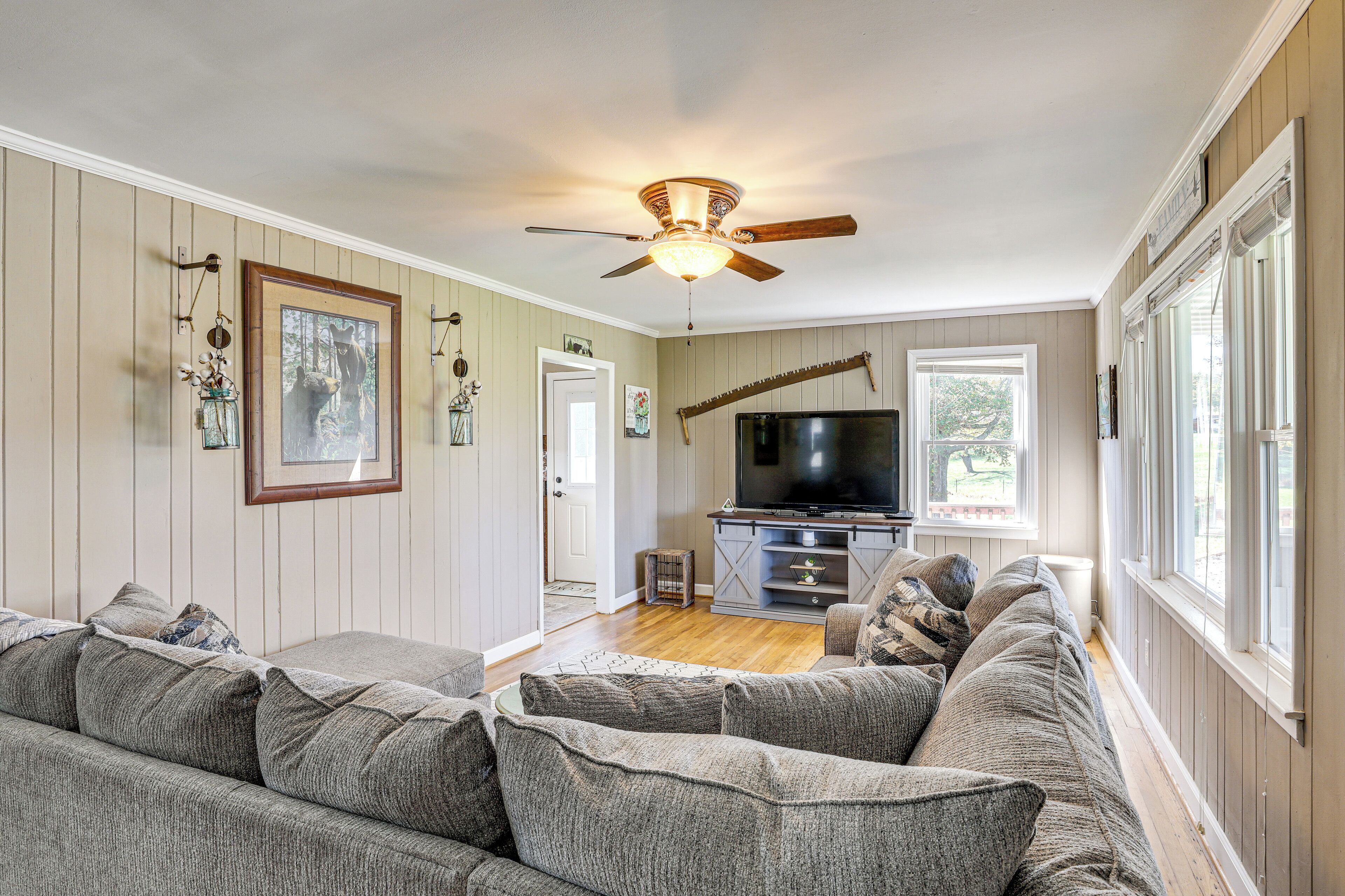 Ein Wohnzimmer mit grauem Ecksofa, Deckenventilator, Flachbildfernseher und Holzboden.