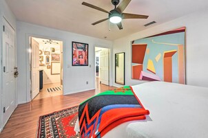 Quarto moderno com cama, ventoinha no teto e uma grande pintura abstrata na parede.