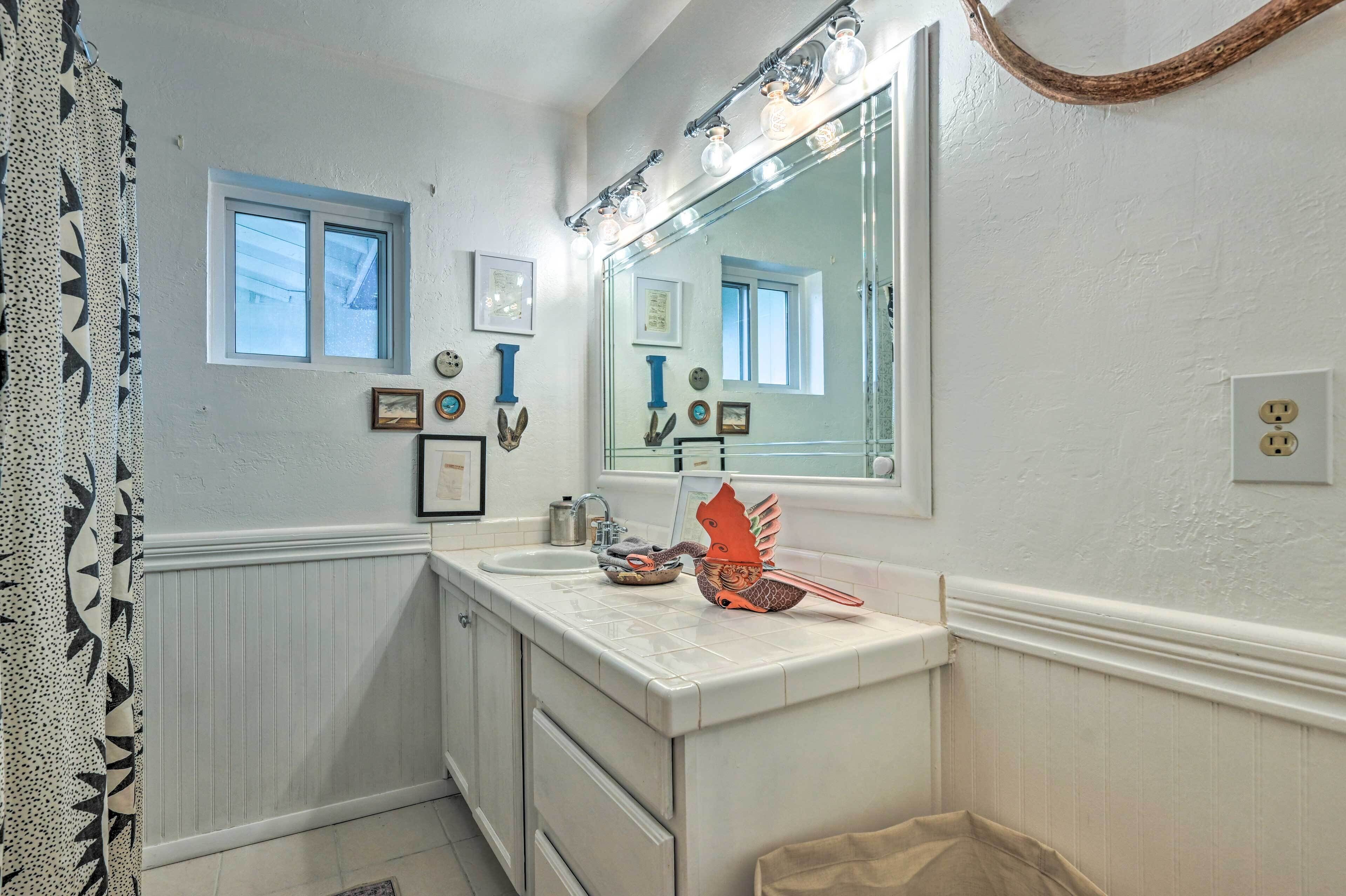 A bathroom with a white vanity, a large mirror, and a window with a view.