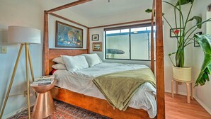 Uma cama com dossel e cabeceira de madeira, um abajur e uma janela ampla com vista para a cidade.