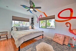 Un dormitorio con cama, un banco de madera, un ventilador de techo y una ventana con vista a árboles.