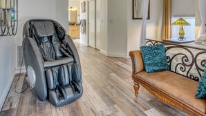 Un fauteuil massant, un canapé agrémenté d’un coussin à volants et une lampe sur une table de chevet.