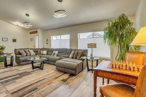 A living room with a sectional sofa, a coffee table, a chess table, and a large plant.