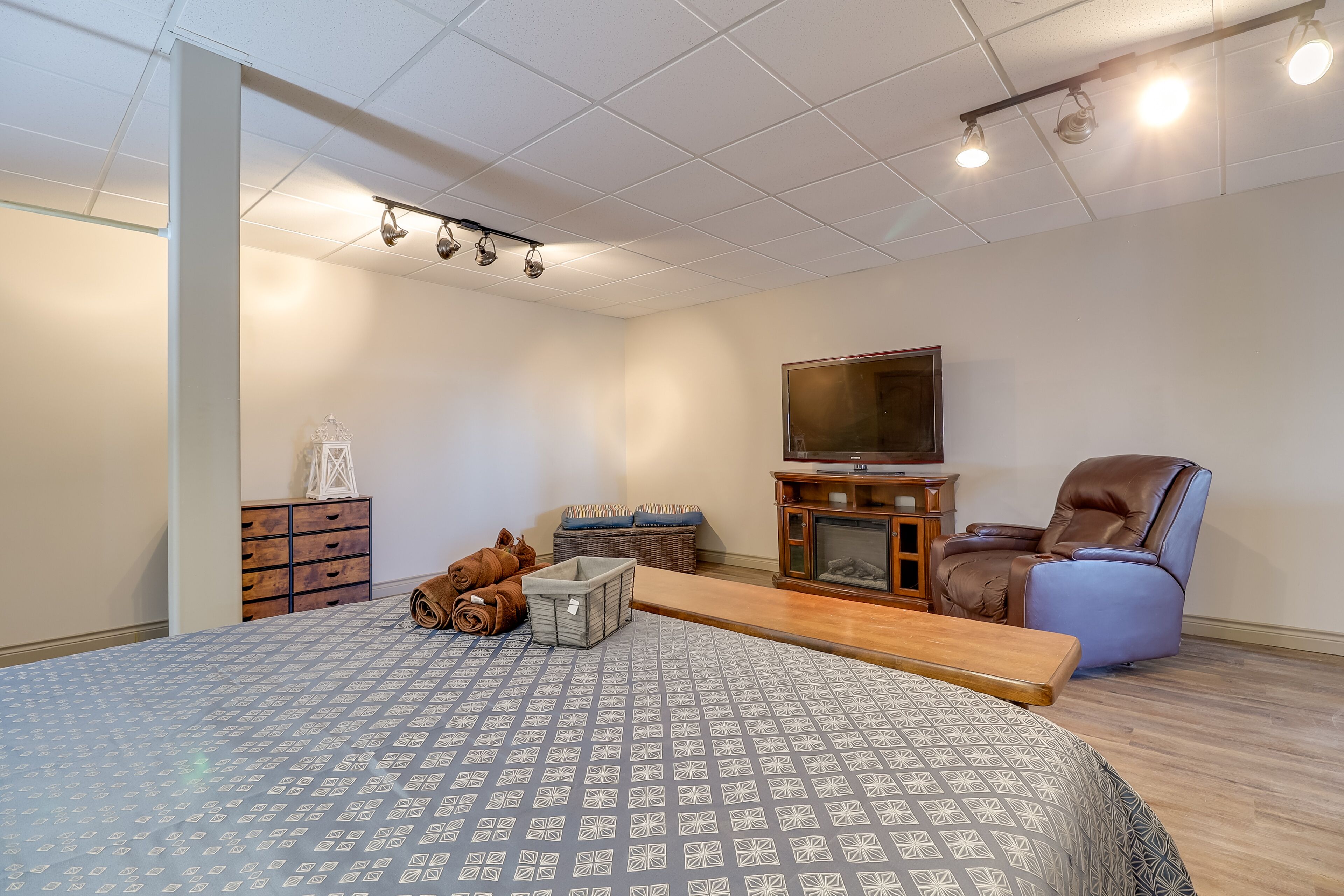 A bedroom with a large bed, a television, a leather recliner, a wooden dresser, and a bench.
