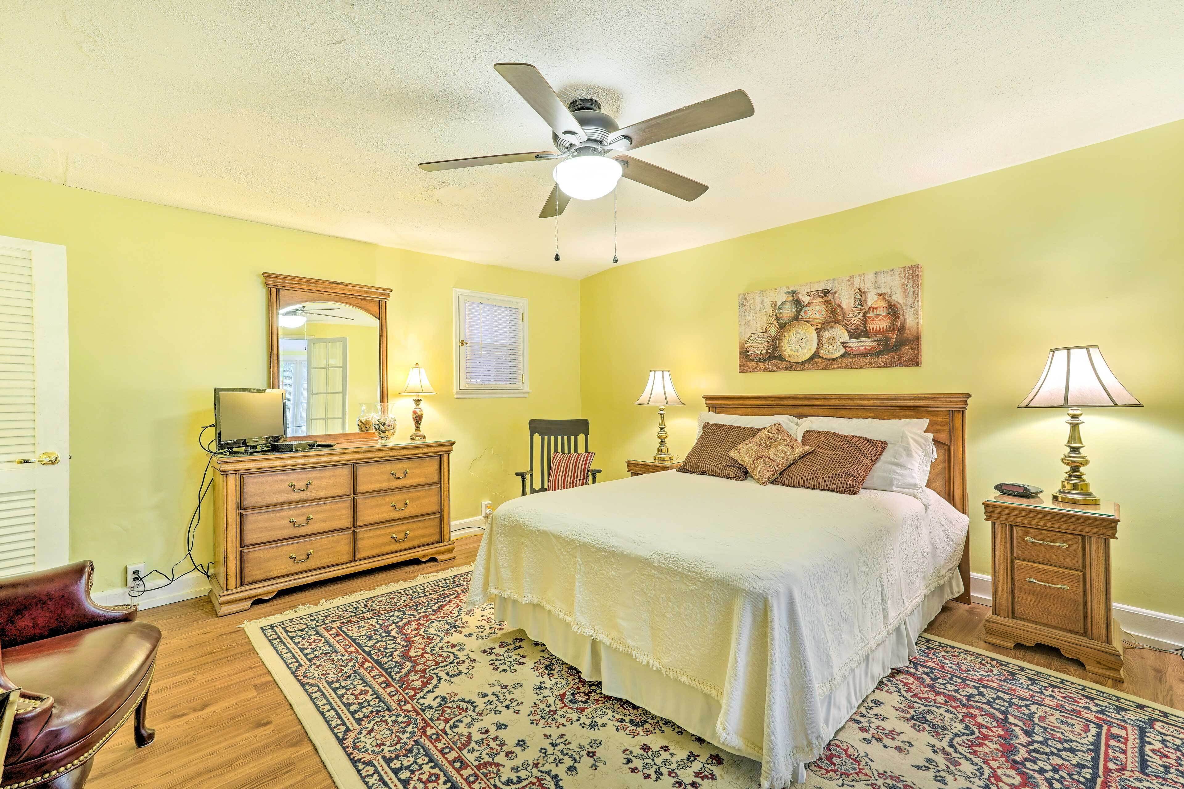 A bedroom with a bed, a ceiling fan, a dresser, a chair, and a nightstand with lamps.