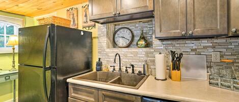 A kitchen with dark wooden cabinets, a black refrigerator, a double sink, and a clock on the wall.
