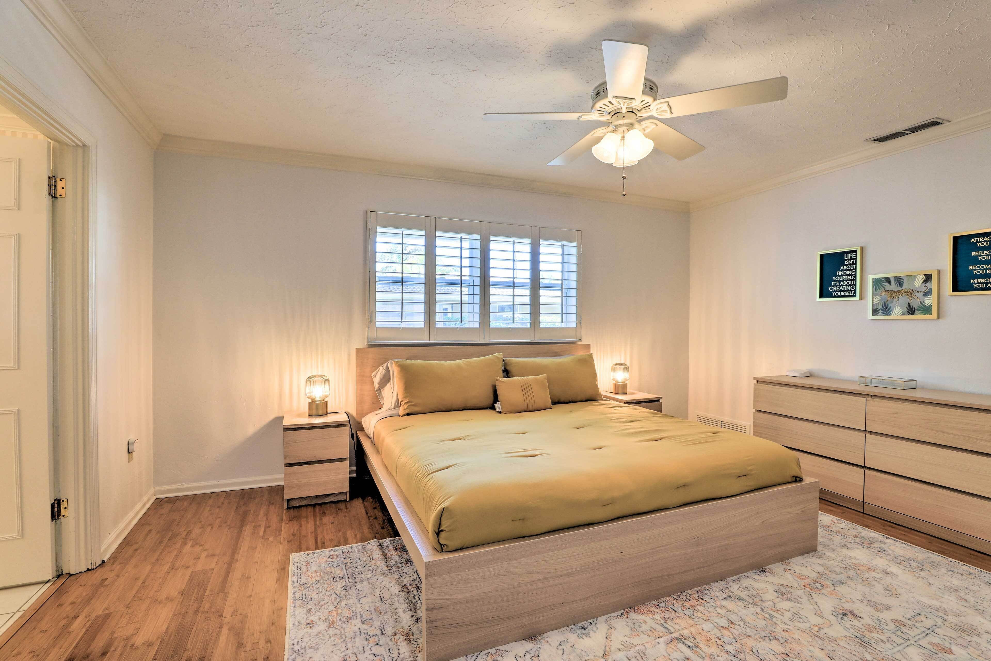 Une chambre à coucher comprenant un lit, des tables de chevet, un ventilateur de plafond, une fenêtre et une commode.