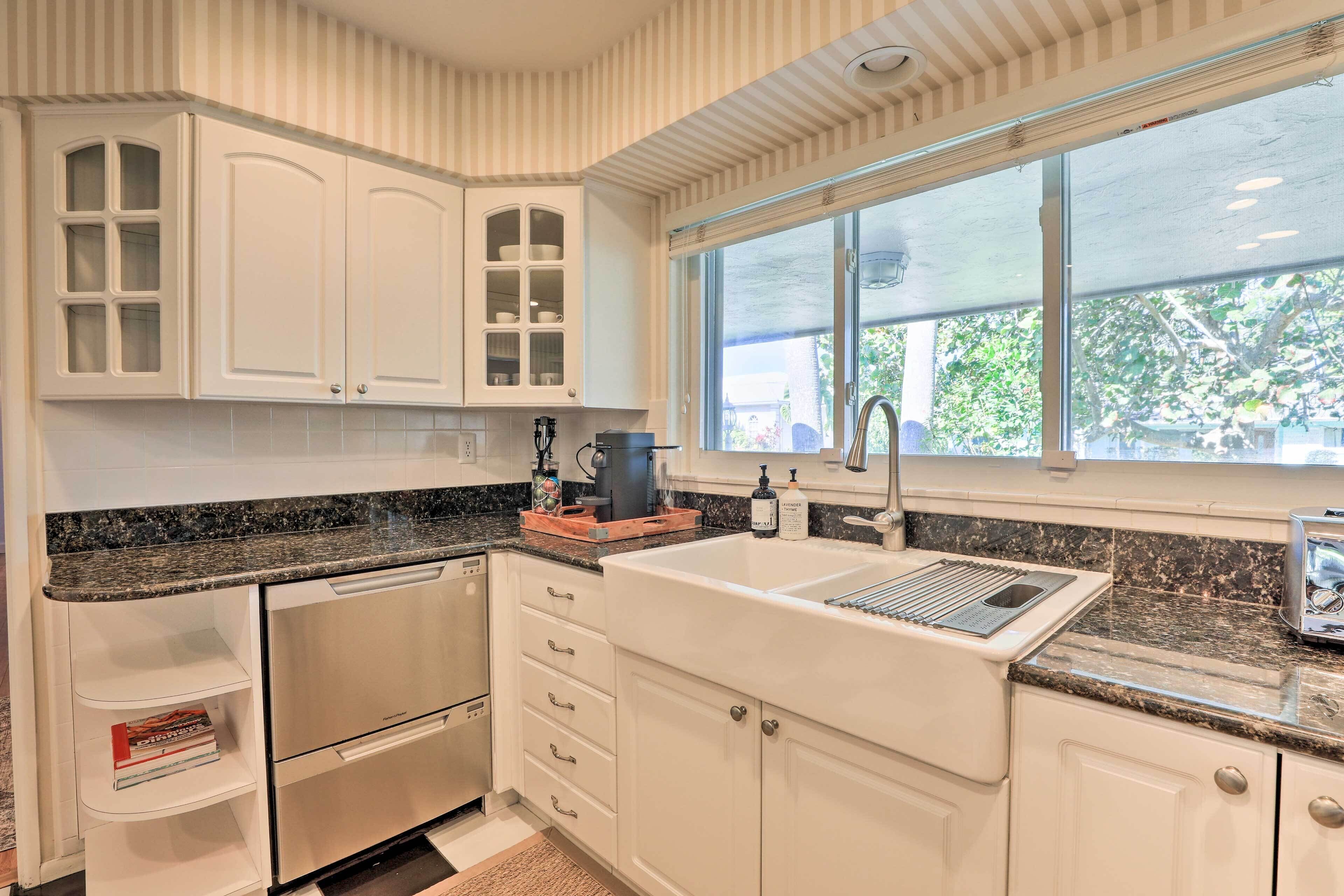 Una cocina con armarios blancos, encimera de granito, lavavajillas integrado y ventana con vistas al exterior.