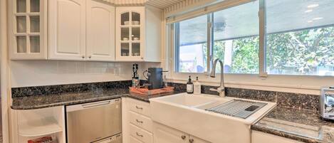 Una cocina con armarios blancos, encimera de granito, lavavajillas integrado y ventana con vistas al exterior.