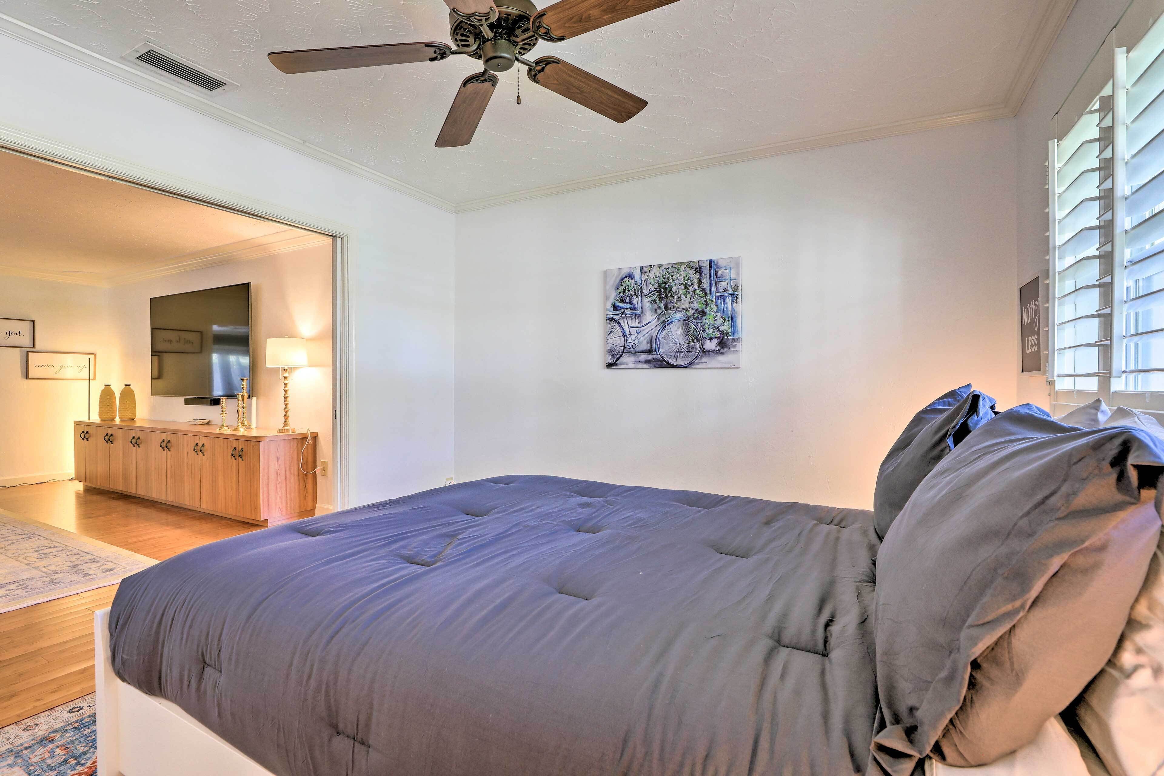 A bedroom with a bed, a ceiling fan, a painting, and a window with blinds.