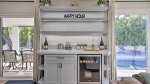 A modern kitchen with a built-in wine fridge, a 'Happy Hour' sign, and a view of the outdoor seating area. - Pool, Jacuzzi & Fire Pit: Scottsdale Escape! (Scottsdale)