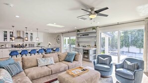 A modern living room with a beige sectional sofa, a wooden coffee table, and two blue armchairs. A kitchen with white cabinets and blue chairs is visible in the background. - Pool, Jacuzzi & Fire Pit: Scottsdale Escape! (Scottsdale)