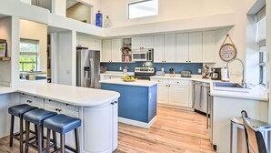 A modern kitchen with white cabinets, a central island with stools, stainless steel appliances, and a view of the outdoors. - Pool, BBQ & Fire Pit: Family Home in Cave Creek (Cave Creek)