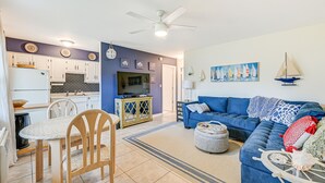 A modern living room with a blue sofa, a dining area with a wooden table and chairs, and a kitchen with white cabinets and a black backsplash. - Marco Island Condo ~ 1 Mi to the Beach! (Marco Island)