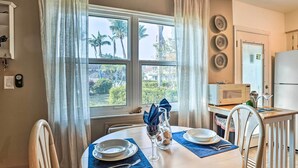 A dining area with a round table, chairs, and a view of palm trees through large windows. - Marco Island Condo ~ 1 Mi to the Beach! (Marco Island)
