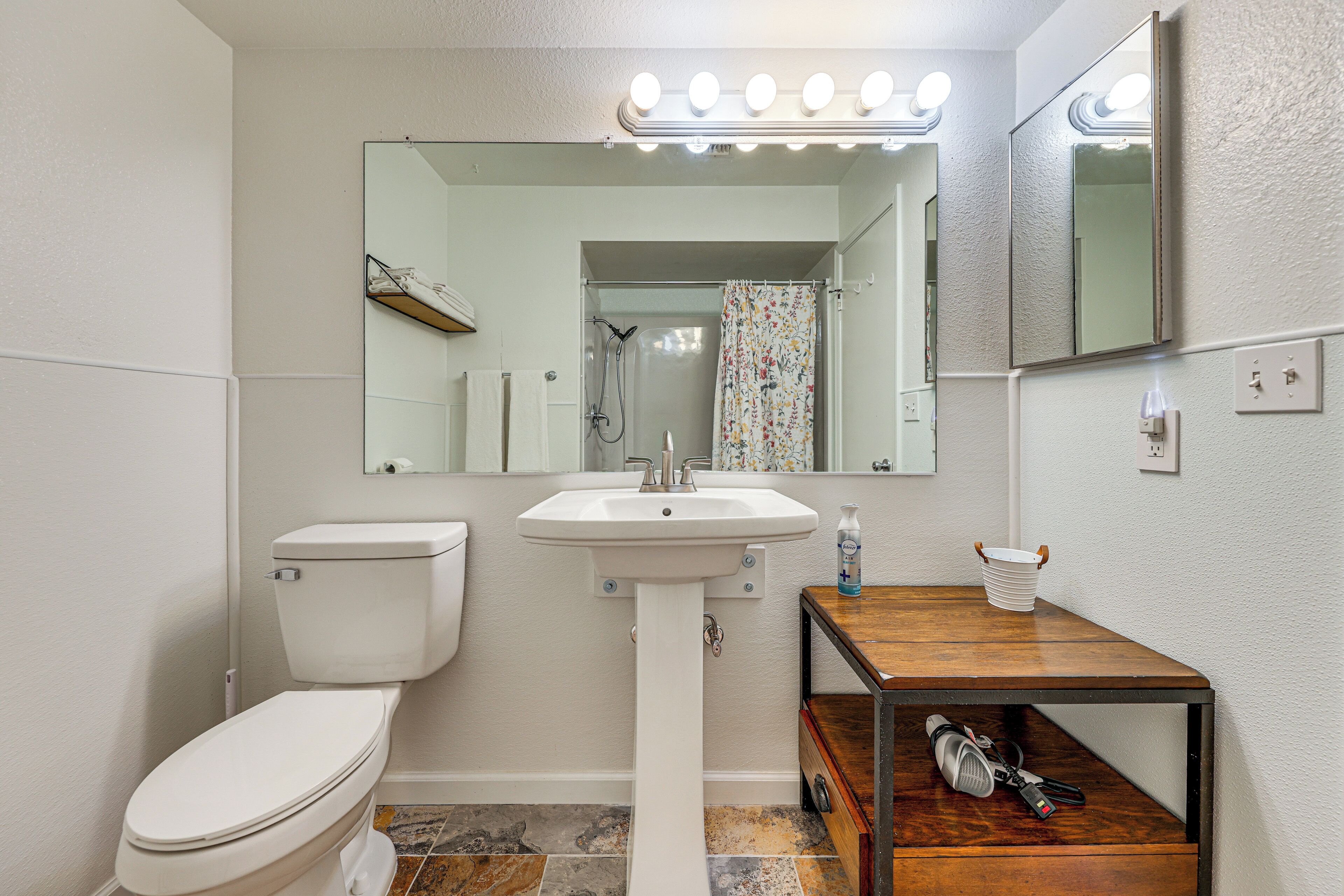 A bathroom with a toilet, sink, mirror, and a shelf with towels.