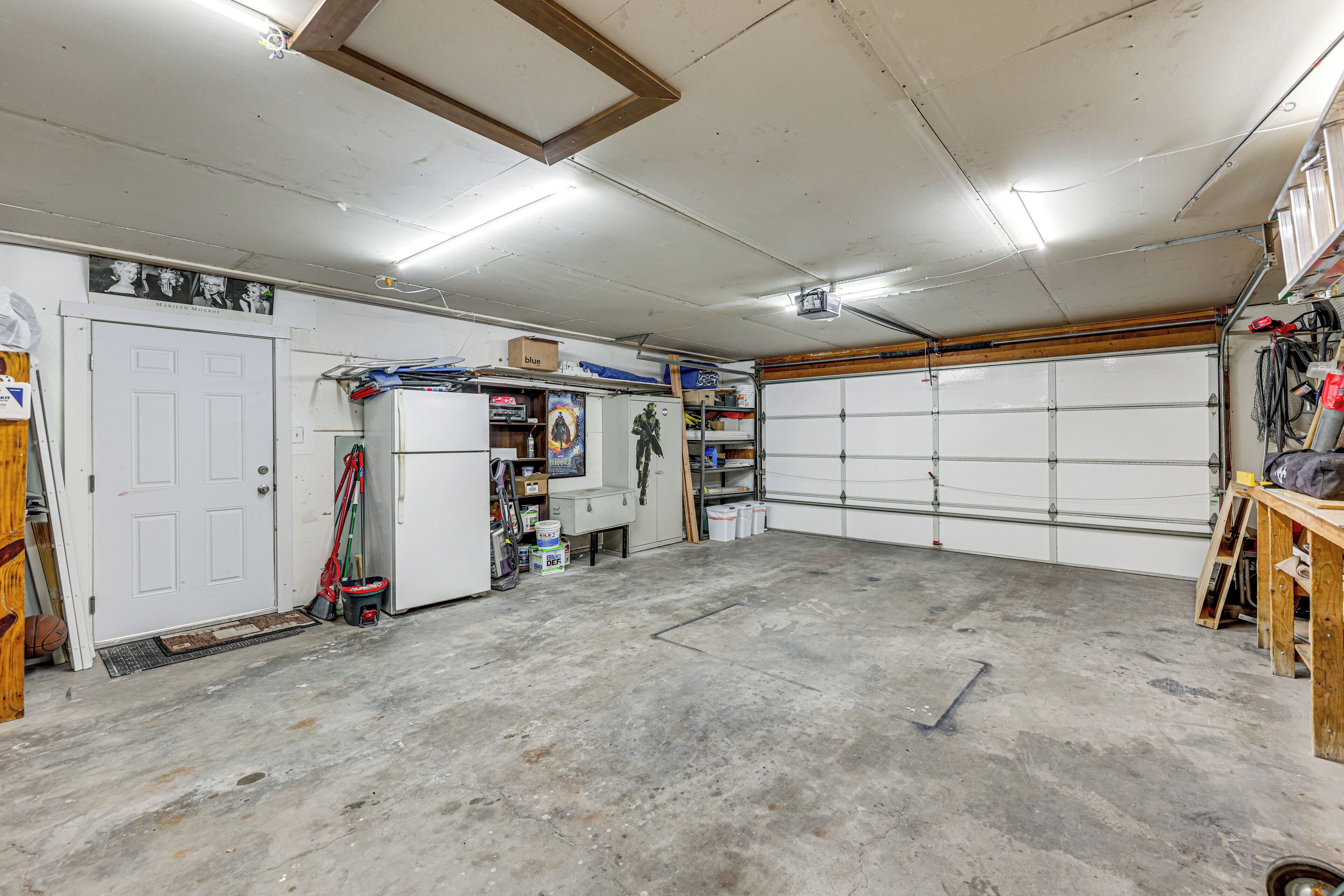 A garage with a concrete floor, a white door, and a closed garage door.