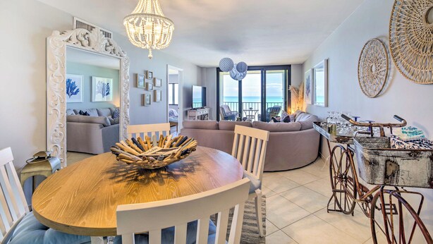 A spacious living area with a round wooden table, white chairs, a chandelier, and a large mirror. - Lovely Fort Pierce Condo, Walk to Beach! (Fort Pierce)