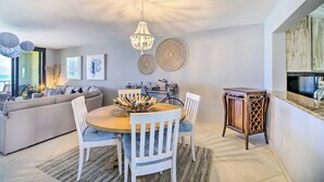 A modern living room with a sofa, dining table, and chairs. There is a chandelier hanging from the ceiling and artwork on the walls. - Lovely Fort Pierce Condo, Walk to Beach! (Fort Pierce)