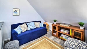 Uma sala de estar aconchegante com um sofá azul, almofadas estampadas, uma mesa lateral de madeira com livros e um tapete tecido.