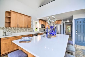Una cocina moderna con armarios de madera, una isla de mármol blanco y un jarrón azul con flores.