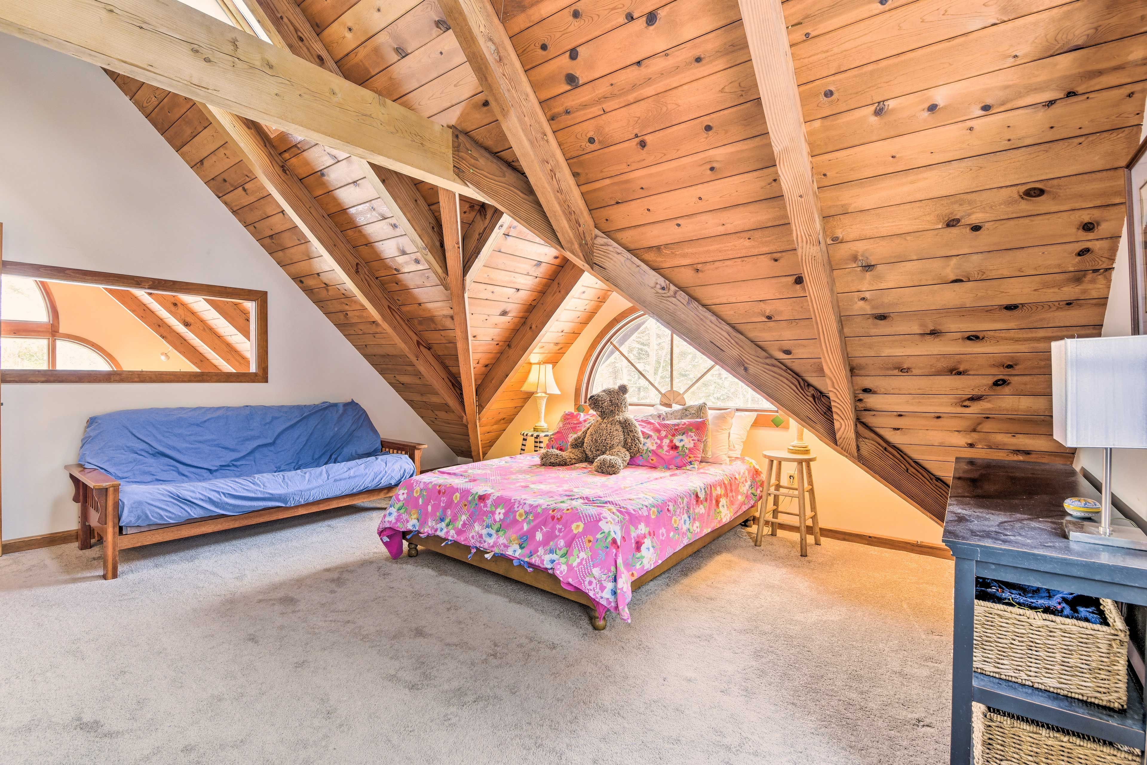 Un dormitorio acogedor en el ático con techo de madera, una cama con colcha estampada, un sofá azul y un osito de peluche.