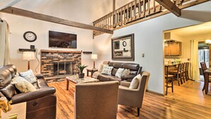 A spacious living room with a fireplace, leather sofas, wooden flooring, and a dining area with wooden furniture.