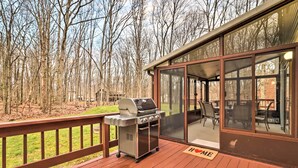 A covered outdoor deck with a grill, a dining area with chairs, and a glass door leading inside.