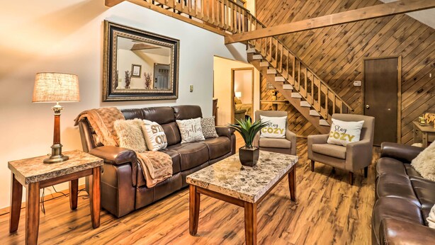 A spacious living room with a brown leather sofa, a coffee table, and a fireplace. A wooden staircase leads to an upper level.
