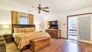 A bedroom with a bed, wooden chest, nightstands, a dresser, a television, and a sliding glass door to the outside.