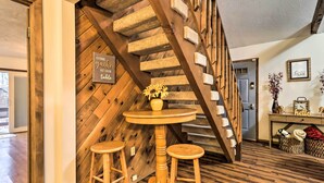 A wooden staircase with a sign that reads "Come gather at our table." A round wooden table with two stools is positioned at the base of the stairs.
