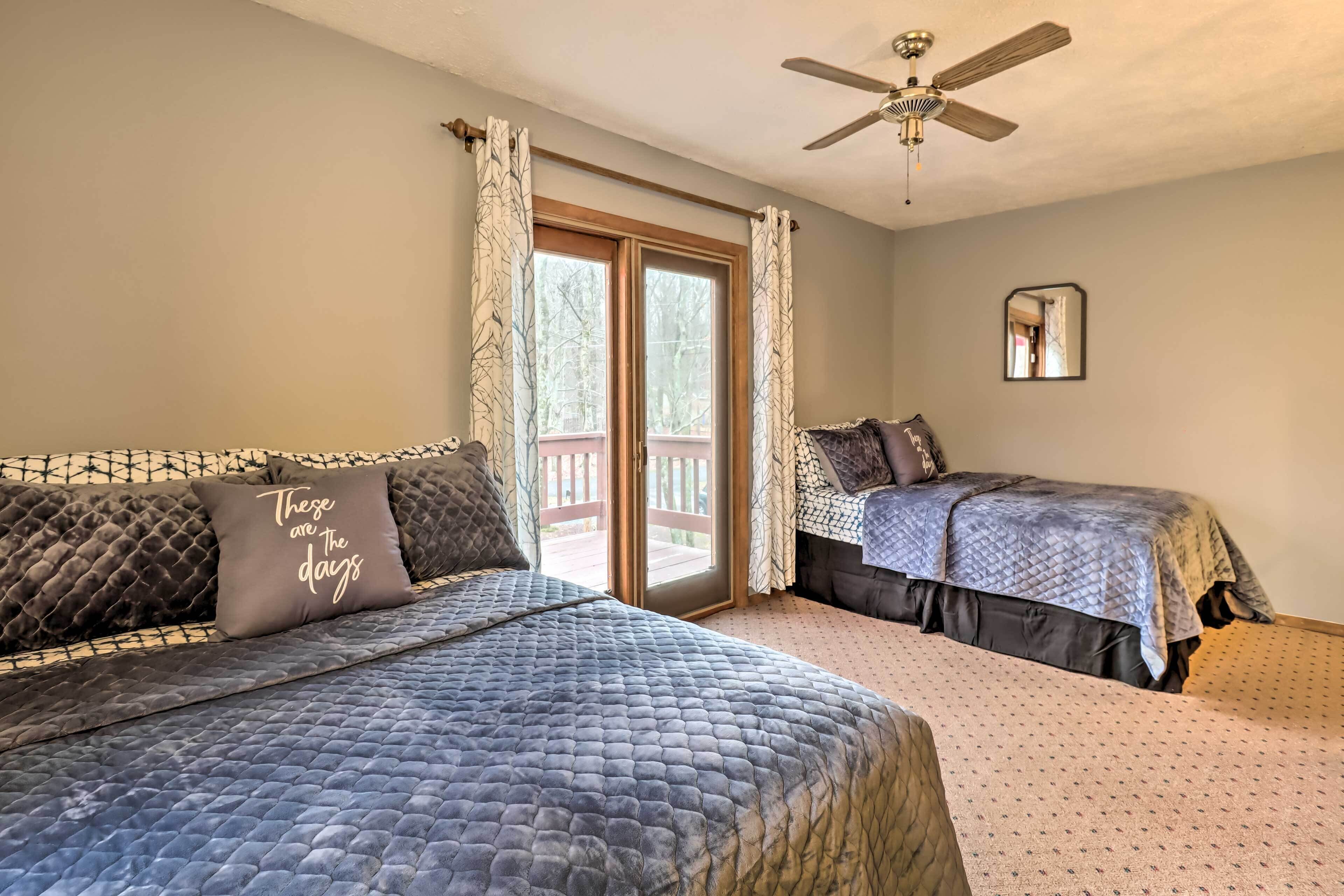 A bedroom with two beds, a ceiling fan, a large window with curtains, and a view of the outdoors.