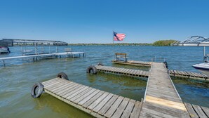 Un muelle de madera que se extiende sobre un lago, con una bandera estadounidense, bancos y una zona cubierta con sillas.