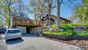 Una casa de dos pisos con un porche de madera, un garaje y un jardín ajardinado con una gran formación rocosa.