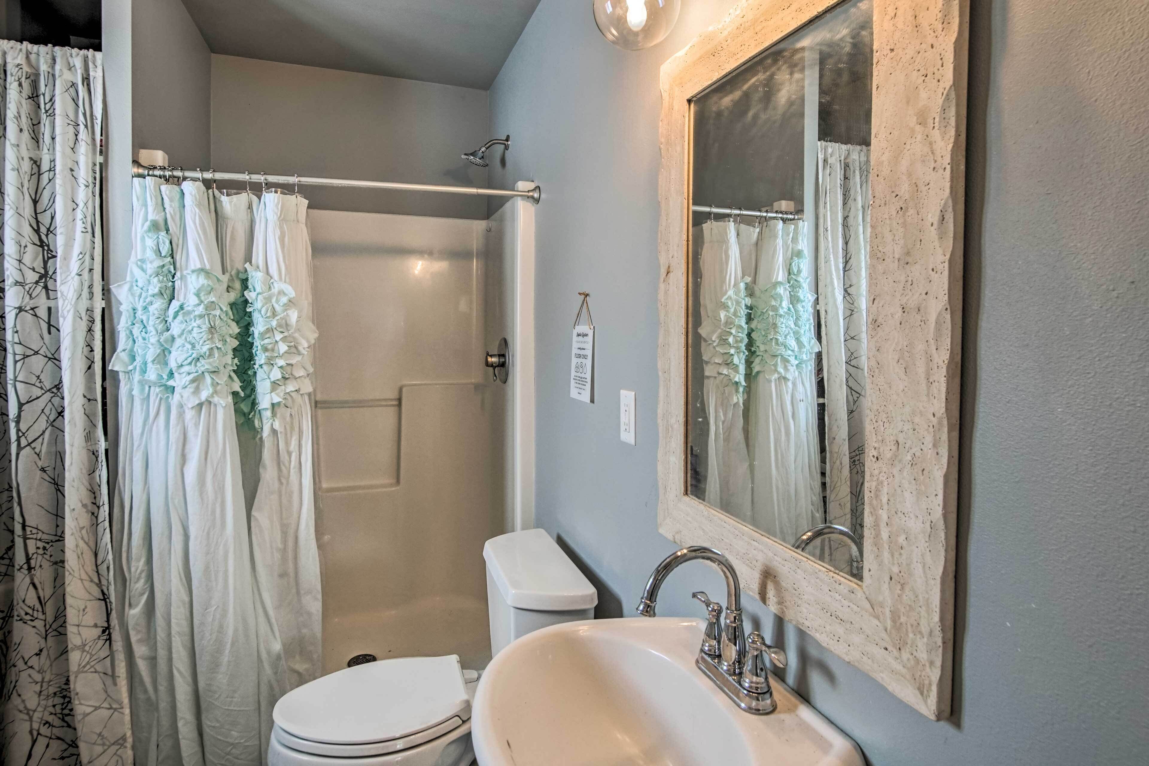 A bathroom with a shower, toilet, sink, and a mirror.