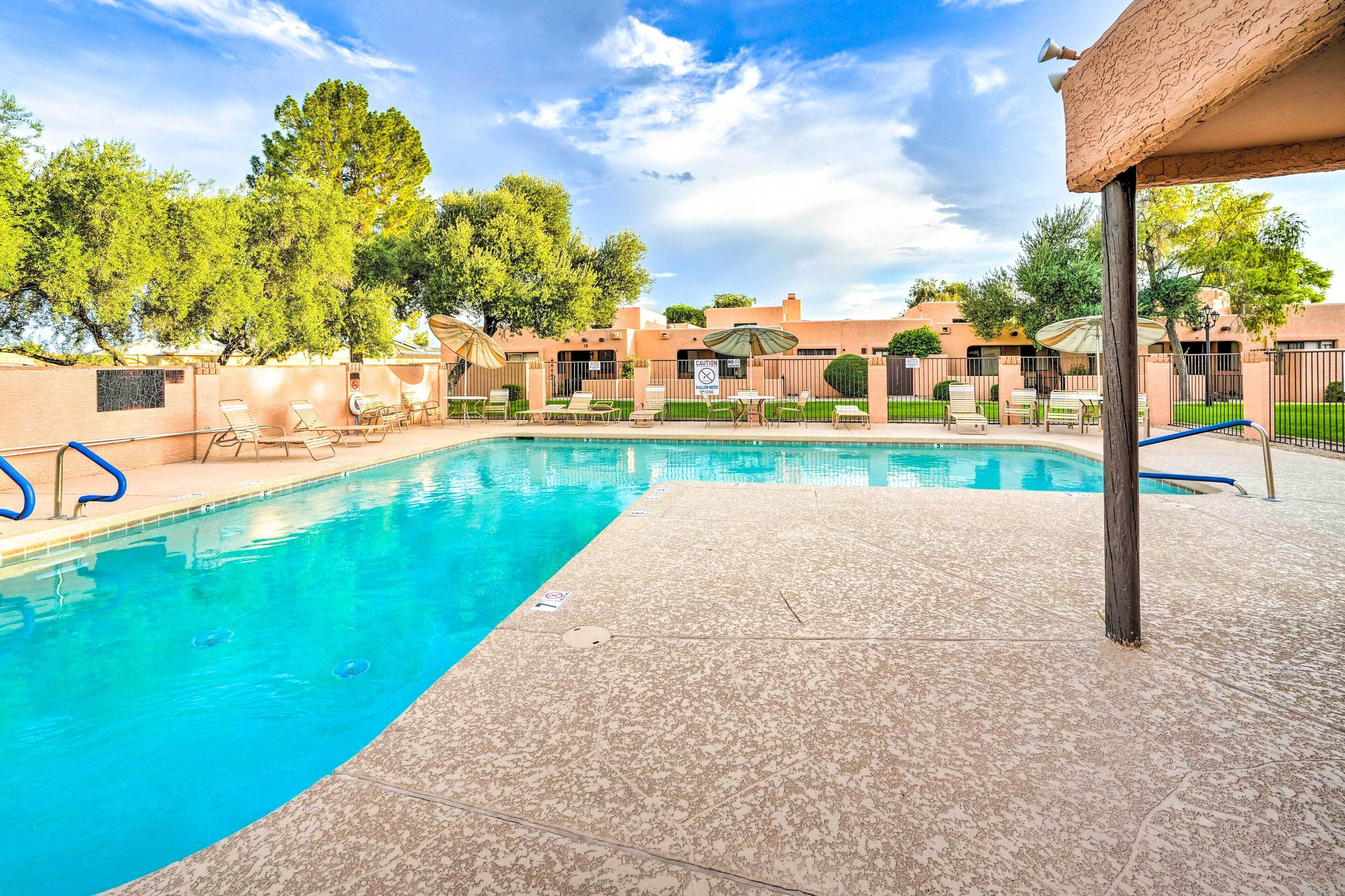 A swimming pool with lounge chairs and umbrellas, surrounded by trees and buildings.