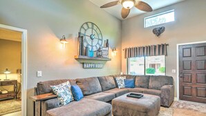 A living room with a sectional sofa, ottoman, decorative wall clock, and a ceiling fan. - Peoria Oasis w/ Resort Amenities, 2 Mi to Downtown (Peoria)